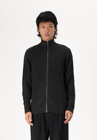 Schwarzer gerippter Strick-Zip-up-Pullover mit hohem Kragen, langen Ärmeln und silbernem Reißverschlussdetail. Glatte Textur, taillierte Passform.