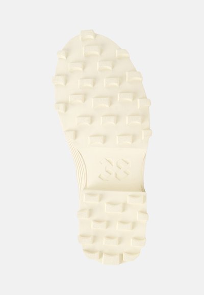 Cream-colored athletic shoe outsole with raised rectangular and triangular lugs for traction. Features smooth edges and a textured surface.