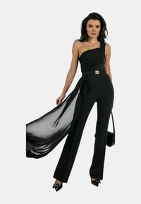 Body nero con design a spalla unica, tessuto fluente su un lato, corpino aderente, accentuato da dettagli dorati in vita e silhouette a gamba larga.