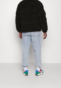 Giacca nera pelosa, jeans di denim azzurro chiaro e sneakers multicolori con accenti di rosso, verde e blu su sfondo bianco.