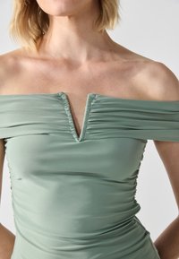 Vestido de hombros descubiertos en suave tejido verde, con una textura fruncida y escote en V, con recogidos laterales ajustados que realzan la silueta.