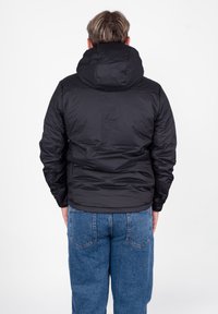 Czarna puchowa kurtka z kapturem, o gładkiej fakturze i pikowanym wzorze. Połączona z niebieskimi dżinsami o swobodnym kroju.