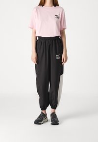 Rosa bomulls-T-shirt med svart Nike-logotyp, ihop med svarta och vita träningbyxor med elastisk midja och muddar, samt svarta sportskor.