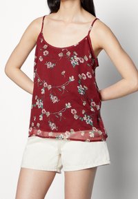 Camiseta sin mangas burdeos con estampado floral, con delicados patrones de flores en rosa y verde. Tejido ligero y semitranslúcido; corte relajado.