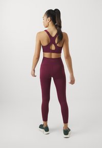 Burgundi sportmelltartó racerback dizájnnal és kivágott részlettel, magasan derekú burgundi leggingssel párosítva, amely hálós részletekkel rendelkezik.