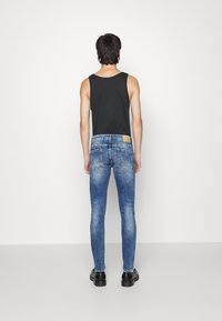 Top sin mangas negro y jeans ajustados azules con un lavado claro, que presentan un parche en la cinturilla trasera y un diseño hasta el tobillo.