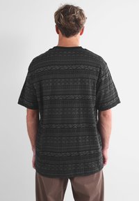 T-shirt nera con motivo geometrico, maniche corte e collo rotondo. Il tessuto appare testurizzato con una vestibilità ampia.