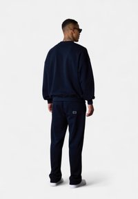 Sweat-shirt bleu marine et joggeurs assortis en tissu doux ; avec des poignets côtelés et un détail de logo au dos du pantalon.