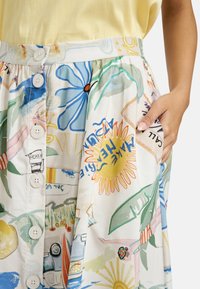 Knieumhangrock aus leichtem, texturiertem Stoff mit einem bunten, verspielten Print von Blumen, Blättern und Sommerschauplätzen, ausgestattet mit Taschen.