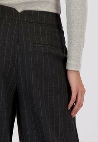 Donkergrijze pinstriped broeken van een gestructureerde stof met zijzakken en een hoge tailleband, gedragen met een lichtgrijze langemouwen top.