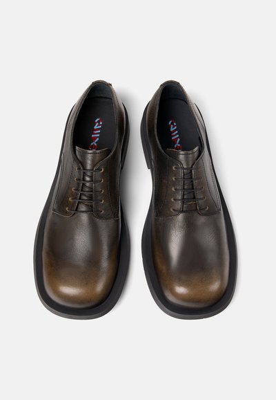 Bruine leren schoenen met een gladde afwerking, ronde punt en zes veterogen. Zwarte rubberen zool en binnenvoering met kleurrijk logo.