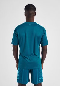 Teal træningsskjorte med korte ærmer og rund hals, parret med matchende shorts med diagonale detaljer og logo på benet.