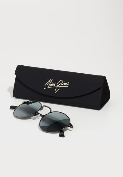 Ochelari de soare Maui Jim cu lentile rotunde negre, rame din metal și vârfuri de ureche texturate, alături de un toc rigid negru cu un logo auriu.