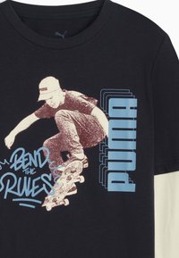 Schwarzes T-Shirt mit kurzen Ärmeln aus Baumwolle. Mit einer Grafik eines Skateboardfahrers und dem Text "BEND THE RULES" in Blau. Puma-Logo am Kragen.