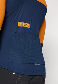 Maillot de cyclisme à manches longues bleu marine et orange avec un dos texturé, une étiquette logo sur le devant et des coutures plates. Matériau évacuant l'humidité.