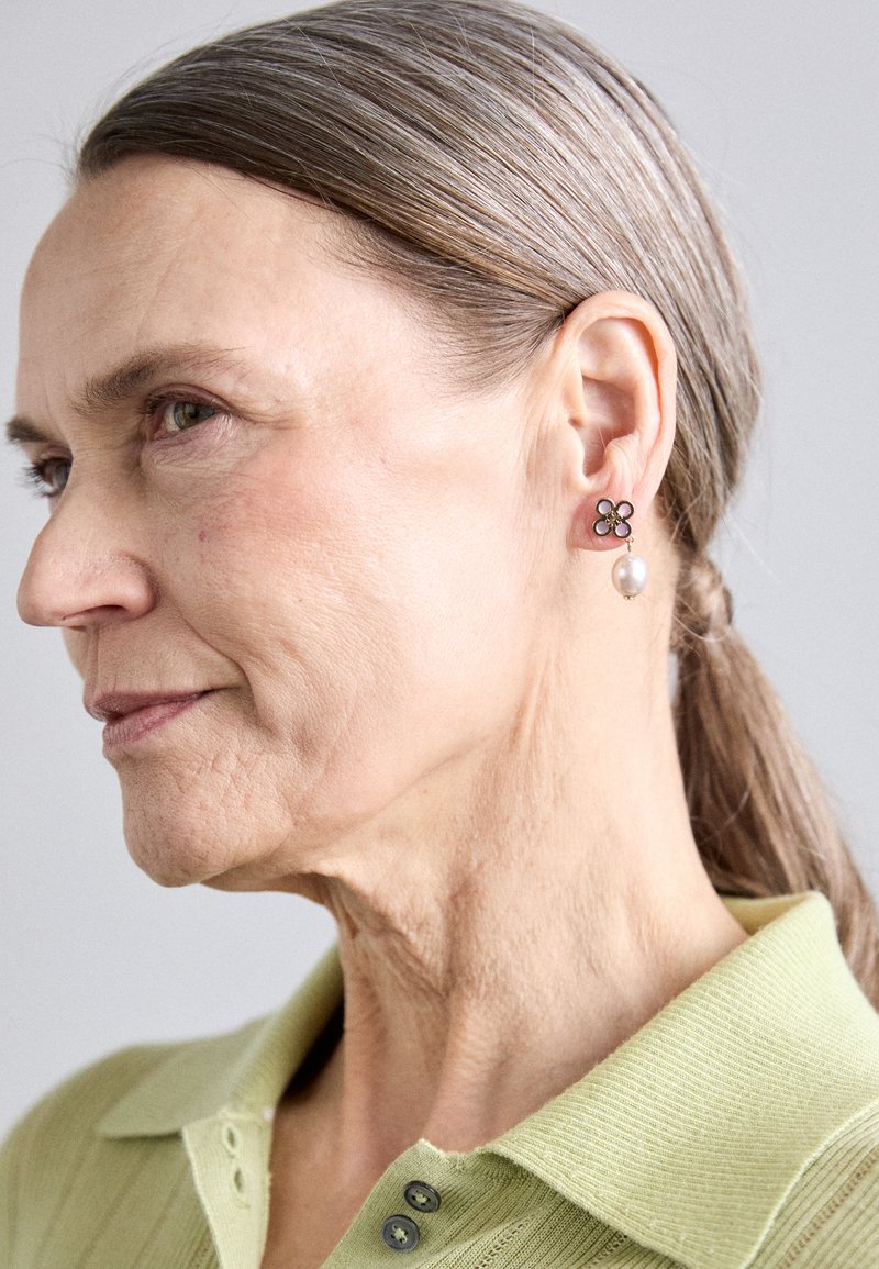 Korvinkuosiset korvakorut, joissa on metallipinta ja helmipudotus. Muotoilussa on vihreitä yksityiskohtia ja kiillotettu pinta.