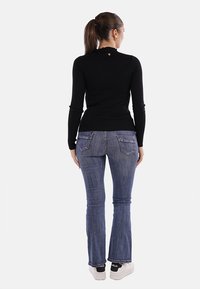 Top lungo a maniche lunghe nero a costine con collo alto, abbinato a jeans flare in denim blu con tasche posteriori e una leggera lavatura.