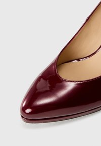 Pompe en cuir verni bordeaux avec un bout pointu et une finition brillante. Présente un décolleté bas et un intérieur lisse.