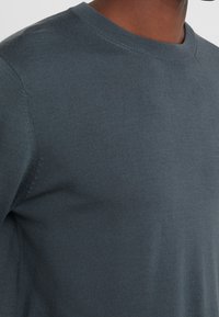 Maglione grigio a collo rotondo in maglia, caratterizzato da una finitura liscia e testurizzata, con dettagli di cucitura visibili sulle cuciture.