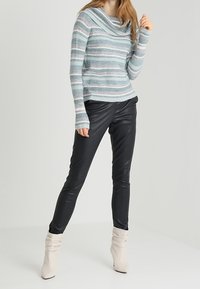 Pull rayé turquoise et gris en maille avec un large col bénitier, associé à un pantalon noir en similicuir et des bottines blanches décontractées.