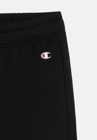 Zwarte joggingbroek van katoen, met een elastische tailleband en een klein geborduurd logo in rood en wit aan de zijkant.