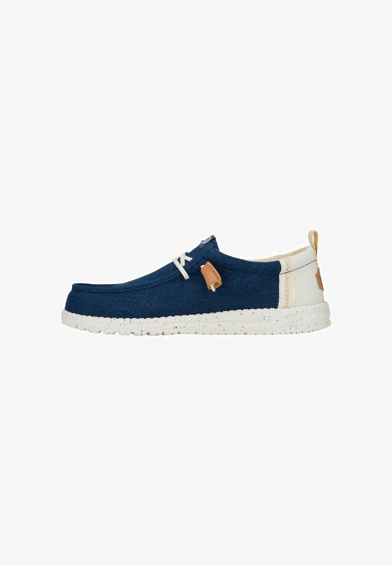 Zapato textil azul marino de tipo slip-on con suela moteada en color off-white, cordones blancos y detalle en color marrón claro, con un diseño que incluye parte trasera y etiquetas laterales cosidas.