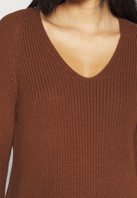 Hnědý pletený svetr s výstřihem do V, který má textura a žebrovanou látku. Žádné viditelné prvky nebo akcenty.