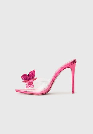 Mule de tacón alto rosa con tira transparente y dos decoraciones de mariposa brillantes en la punta sobre un fondo blanco.
