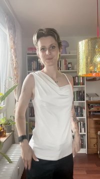 Weißes ärmelloses Oberteil mit einem Wasserfallausschnitt, glattem Stoff, figurbetonter Form und einem leichten Fall, kombiniert mit schwarzen Hosen.