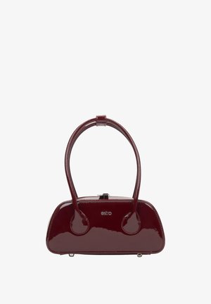 Červená kabelka z lakované kůže s zakřiveným tvarem, dvěma zaoblenými držadly a uzávěrem na patent. Na přední straně má vyražené logo značky.