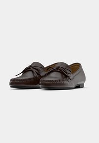 Καφέ δερμάτινα μοκασίνια με στρογγυλεμένη μύτη, διακοσμητική ραφή και φιόγκο στο πάνω μέρος.  Επίπεδες σόλες και λεία υφή.