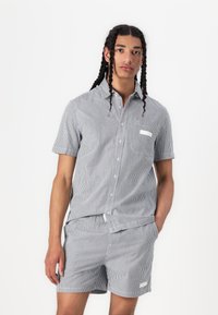 Ensemble chemise boutonnée à manches courtes et short à rayures verticales bleues et blanches. Comprend une poche poitrine et un accent d'étiquette blanche unie.