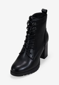 Botines negros de piel lisa, con punta redondeada, ojales metálicos, cordones y un tacón grueso. Suela de goma texturizada.