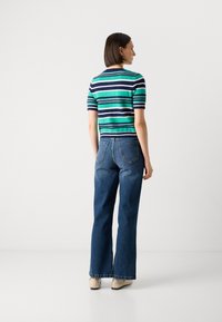 Haut à manches courtes, rayé en vert, marine et blanc, associé à un jean flare taille haute, bleu clair. Design simple et texture solide.