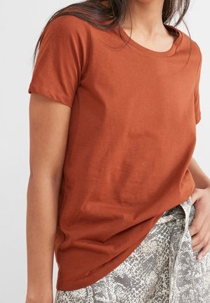 Woman wearing a rust-colored short-sleeve T-shirt tucked into high-waisted pants with a gray and white snake print pattern.