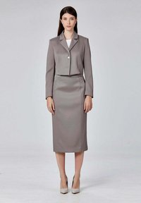 Blazer gris ajusté avec un seul bouton, associé à une jupe crayon assortie. Texture de tissu lisse et longueur mi-mollet. Talons de couleur neutre.