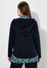 Felpa navy con texture a motivo foglia, con bordatura coordinata in teal, crema e verde all'orlo e al cappuccio posteriore.