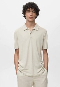 Camisa polo de manga corta beige con cuello, con tapeta de dos botones y textura suave, combinada con pantalones de color claro. Diseño simple y minimalista.