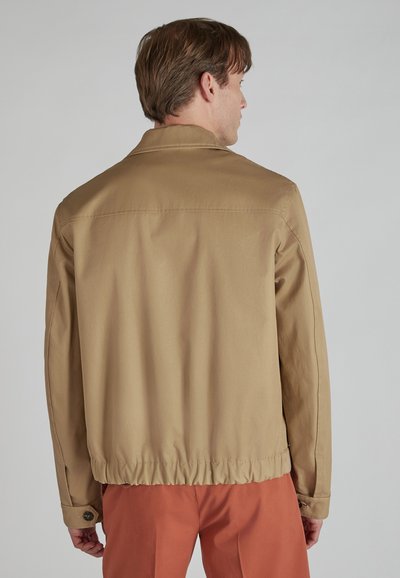 Chaqueta ligera de color marrón claro, con cuello, cintura elástica y puños abotonados, confeccionada en tejido suave. Vista trasera mostrada.