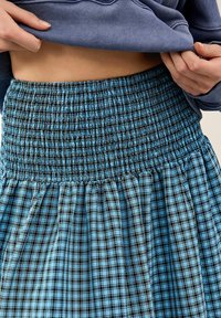 Gonna a quadri blu con vita arricciata. Il tessuto presenta un motivo testurizzato con diverse sfumature di blu e nero.