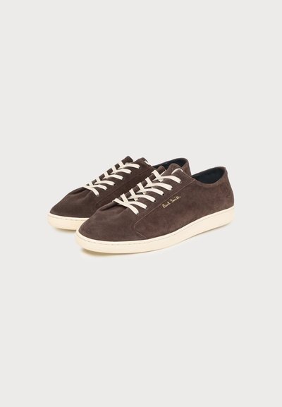 Paire de baskets basses en daim marron avec lacets et semelles écru, détail signature doré, sur un fond clair uni.