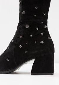 Musta mokkanahkasaapas, jossa on paksu korko, koristeena erilaisia hopeapainatuksia tähden, timantin, ympyrän ja kukan muodoissa.