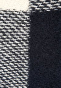 Gros plan sur un tissu en laine montrant des motifs tricotés noirs et blancs avec une surface texturée et duveteuse ainsi qu'une section noire unie.
