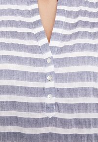 Camiseta de rayas azules y blancas, con escote en pico, rayas horizontales y tres botones en la parte frontal. Hecha de una tela ligera con acabado texturizado.