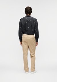 Chemise noire à fines rayures avec de petites figures colorées ; associée à un pantalon beige et des baskets blanches. Vue de dos montrant une coupe décontractée et une ceinture élastique.