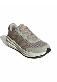 Scarpa sportiva grigio chiaro con pannelli in rete beige, dettagli testurizzati e marchio a tre strisce. Punta rotonda e suola bianca ammortizzata.