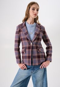 Blazer met houndstooth-patroon in kastanjebruin en blauw, voorzien van een enkele knoop, twee voorzakken en een reverskraag, gecombineerd met een lichtblauw shirt.