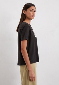 Schwarzes T-Shirt mit kurzen Ärmeln, lockerem Schnitt, Rundhalsausschnitt und dezentem Logodesign auf der Vorderseite. Weiches Baumwollmaterial mit glatter Textur.