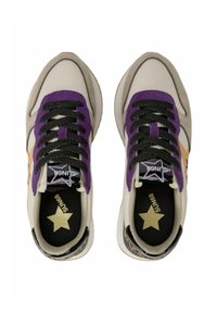 Zapatillas con un upper de tela beige, detalles en ante gris, cordones morados y un logo de estrella dorada en una plantilla negra. Suela de goma con detalle estampado.