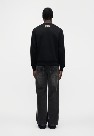 Μαύρο φούτερ με ριμπ μανσέτες, με λογότυπο στην πλάτη. Συνδυασμένο με χαλαρά, σκούρα τζιν. Απλός, μινιμαλιστικός σχεδιασμός.